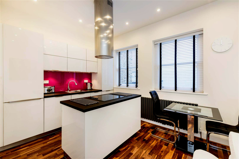 Contemporary single-wall kitchen/diner in London with glass-front cabinets, white cabinets, pink splashback, glass sheet splashback and an island.