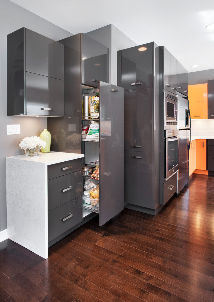 Modern inredning av ett stort kök, med en undermonterad diskho, släta luckor, grå skåp, bänkskiva i kvarts, grått stänkskydd, rostfria vitvaror, mörkt trägolv och en köksö