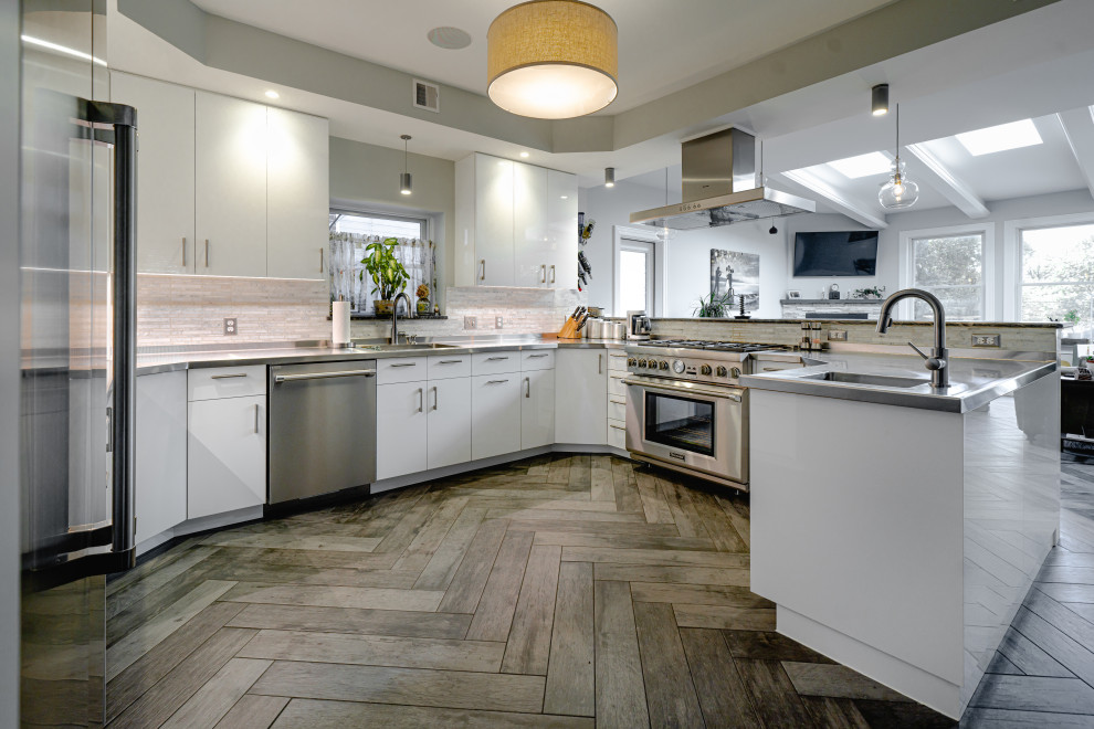 Inspiration for a mid-sized modern u-shaped medium tone wood floor, gray floor and vaulted ceiling eat-in kitchen remodel in Other with a single-bowl sink, flat-panel cabinets, white cabinets, stainless steel countertops, beige backsplash, ceramic backsplash, stainless steel appliances, a peninsula and gray countertops