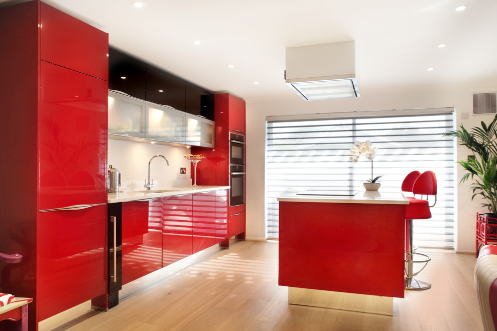 This is an example of a medium sized contemporary single-wall kitchen/diner in Buckinghamshire with an integrated sink, red cabinets, quartz worktops, stainless steel appliances, light hardwood flooring, an island and flat-panel cabinets.
