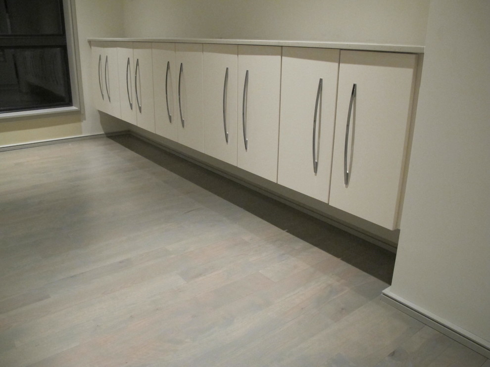 Example of a mid-sized minimalist l-shaped light wood floor kitchen design in Kansas City with flat-panel cabinets, white cabinets, stainless steel appliances and an island