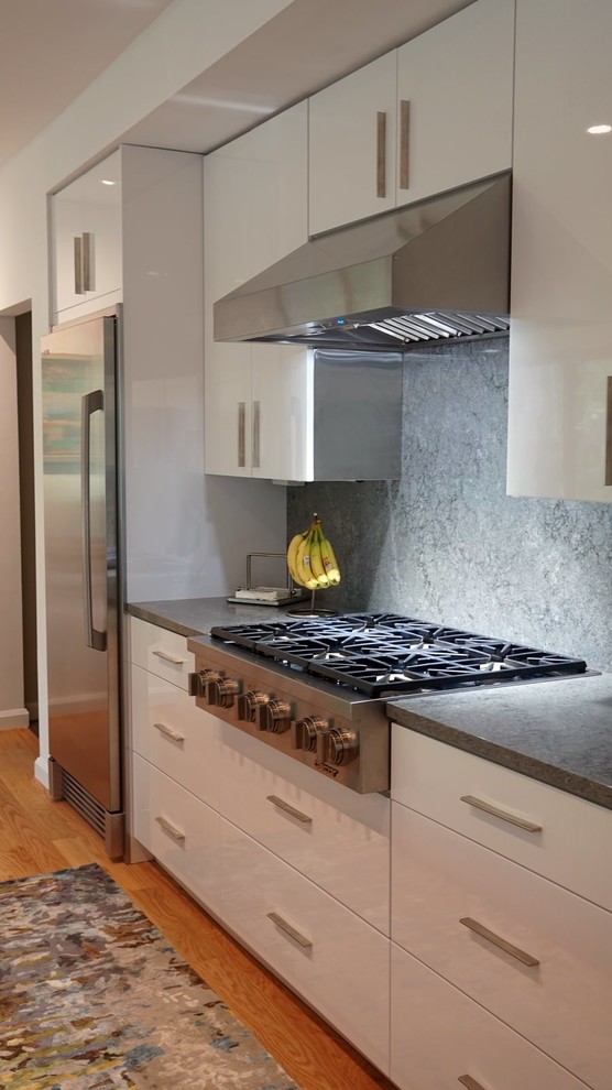 Bild på ett mycket stort funkis grå grått kök, med en undermonterad diskho, släta luckor, vita skåp, granitbänkskiva, grått stänkskydd, rostfria vitvaror, flera köksöar och orange golv