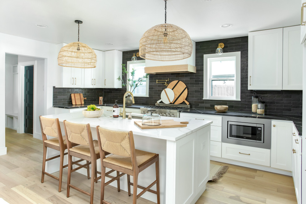 This is an example of a large traditional u-shaped kitchen in Dallas with a submerged sink, shaker cabinets, white cabinets, black splashback, stainless steel appliances, light hardwood flooring, an island, beige floors and black worktops.