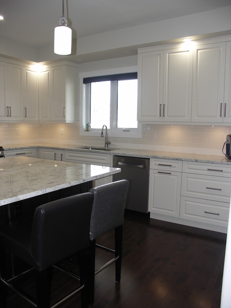 Photo of a large classic l-shaped enclosed kitchen in Edmonton with a submerged sink, raised-panel cabinets, beige cabinets, granite worktops, beige splashback, metro tiled splashback, stainless steel appliances, medium hardwood flooring, an island and brown floors.