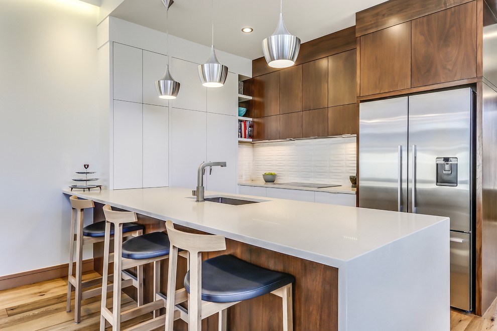 Eat-in kitchen - mid-sized 1960s l-shaped medium tone wood floor eat-in kitchen idea in Calgary with a single-bowl sink, flat-panel cabinets, white cabinets, quartz countertops, white backsplash, ceramic backsplash, stainless steel appliances and a peninsula