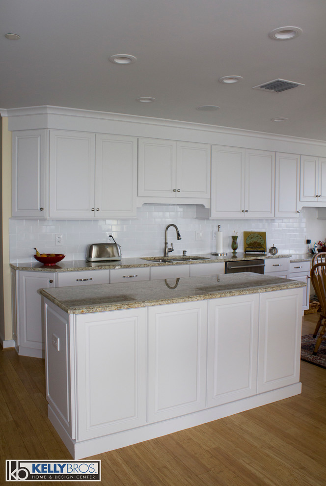 Example of a large transitional light wood floor eat-in kitchen design in Cincinnati with a double-bowl sink, raised-panel cabinets, white cabinets, granite countertops, white backsplash, subway tile backsplash, stainless steel appliances and an island