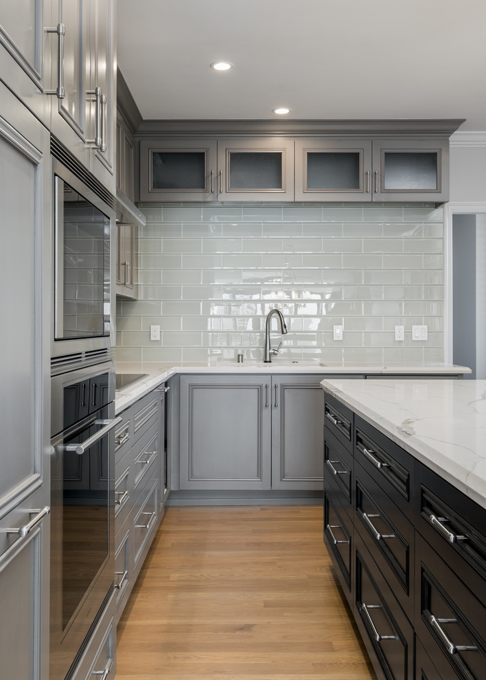 Bild på ett stort funkis vit vitt kök, med en integrerad diskho, luckor med upphöjd panel, grå skåp, granitbänkskiva, vitt stänkskydd, stänkskydd i tunnelbanekakel, rostfria vitvaror, mellanmörkt trägolv, en köksö och brunt golv