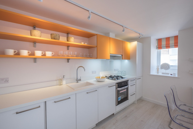 Foto på ett litet funkis linjärt kök med öppen planlösning, med en integrerad diskho, släta luckor, orange skåp, bänkskiva i koppar, vitt stänkskydd, stänkskydd i glaskakel, integrerade vitvaror och målat trägolv