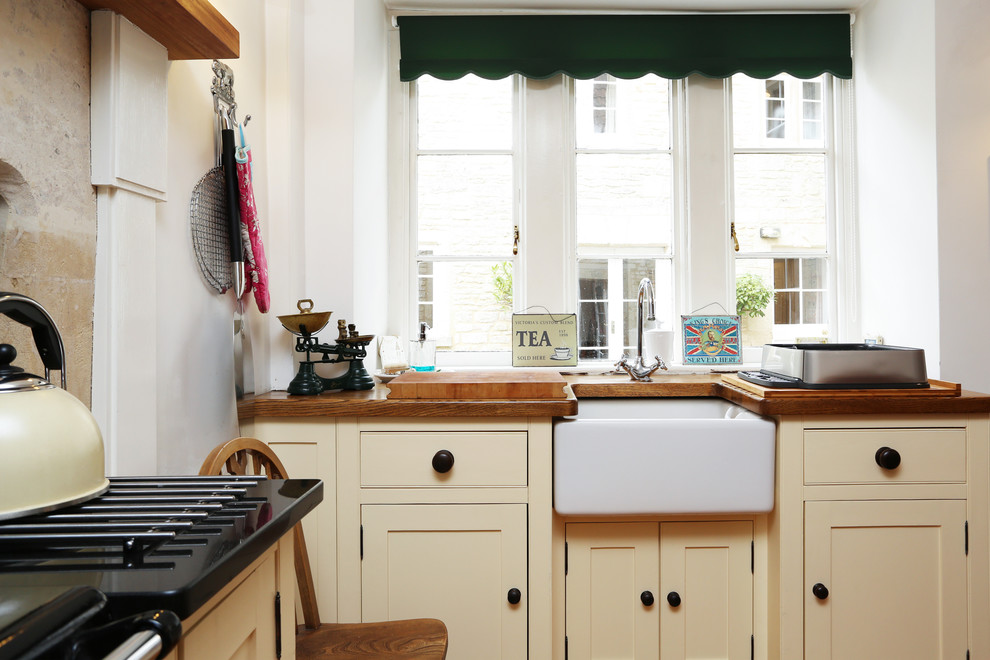 Photo of a small classic l-shaped kitchen/diner in London with a belfast sink, raised-panel cabinets, wood worktops, no island, brown worktops and beige cabinets.