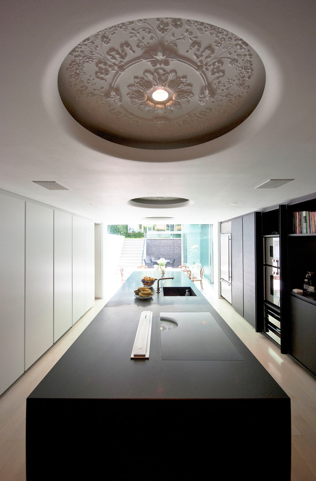 Inspiration for a contemporary galley enclosed kitchen in London with an integrated sink, flat-panel cabinets, black cabinets, stainless steel appliances, an island and beige floors.