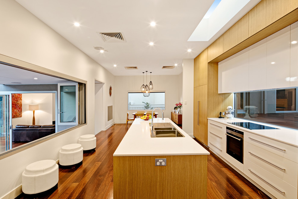 Moderne Küche mit Einbauwaschbecken, flächenbündigen Schrankfronten, weißen Schränken, Rückwand aus Glasfliesen, Küchengeräten aus Edelstahl, dunklem Holzboden und Kücheninsel in Adelaide