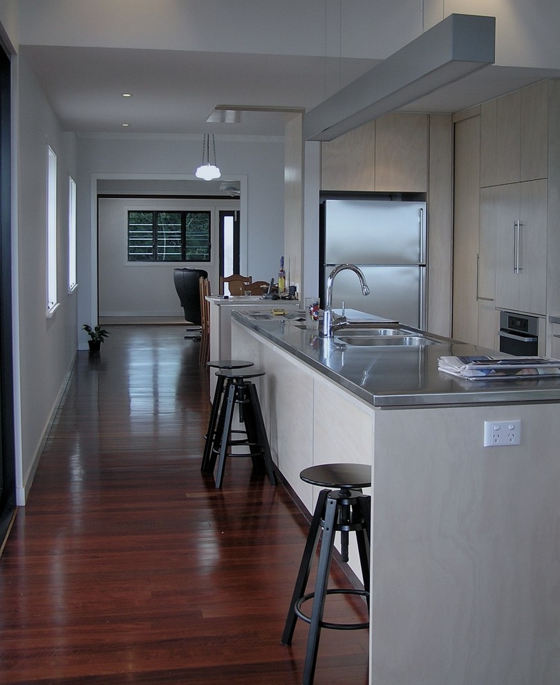 Cette image montre une cuisine parallèle design en bois clair avec un évier 2 bacs, un placard à porte plane, un plan de travail en inox et un électroménager en acier inoxydable.