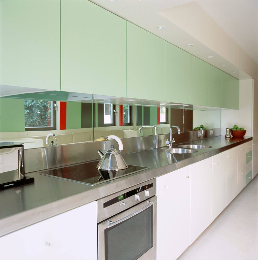 Design ideas for a small modern galley kitchen/diner in London with a built-in sink, flat-panel cabinets, white cabinets, stainless steel worktops, green splashback, mirror splashback, white appliances, ceramic flooring and no island.