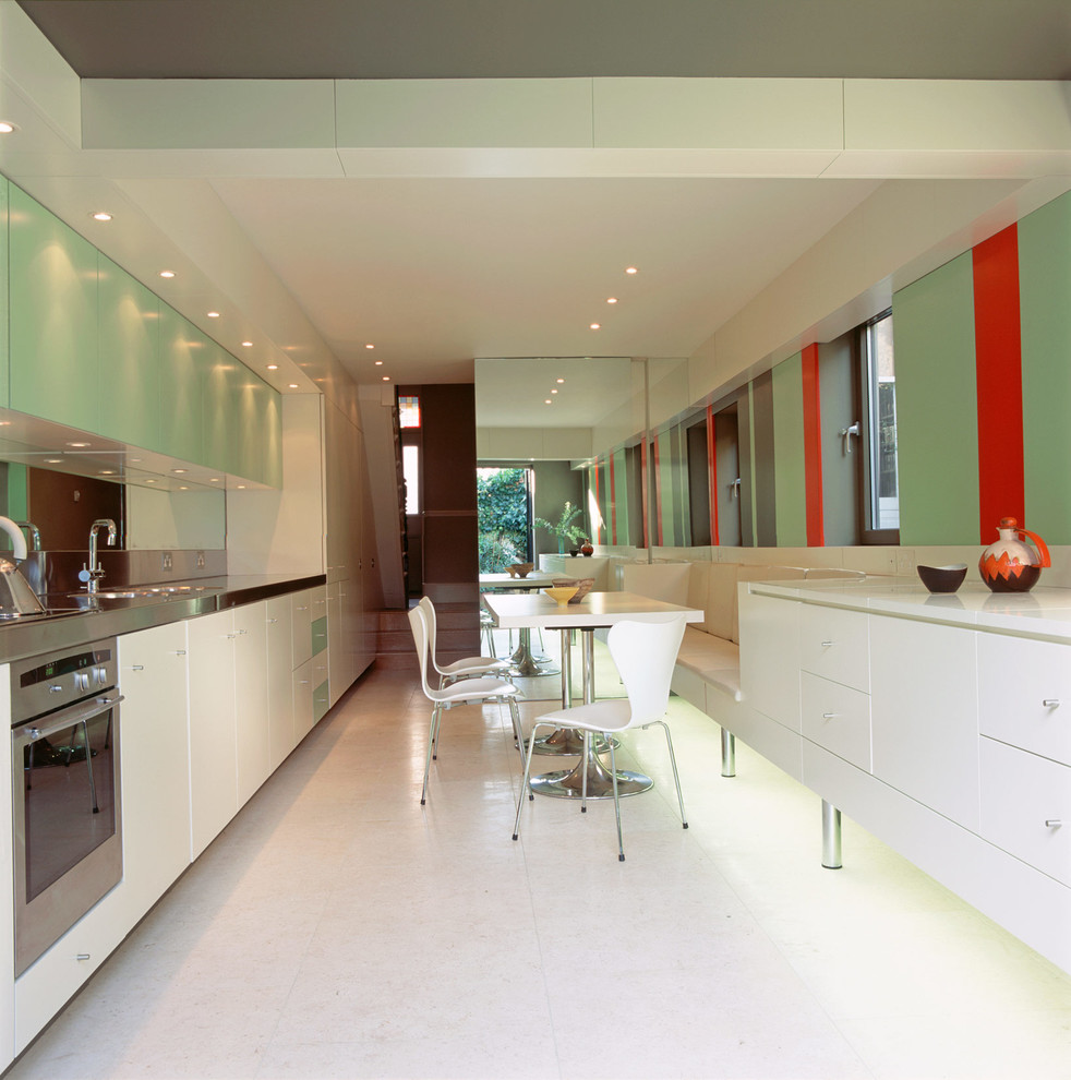 Small modern galley kitchen/diner in London with a built-in sink, flat-panel cabinets, white cabinets, stainless steel worktops, green splashback, mirror splashback, white appliances, ceramic flooring and no island.