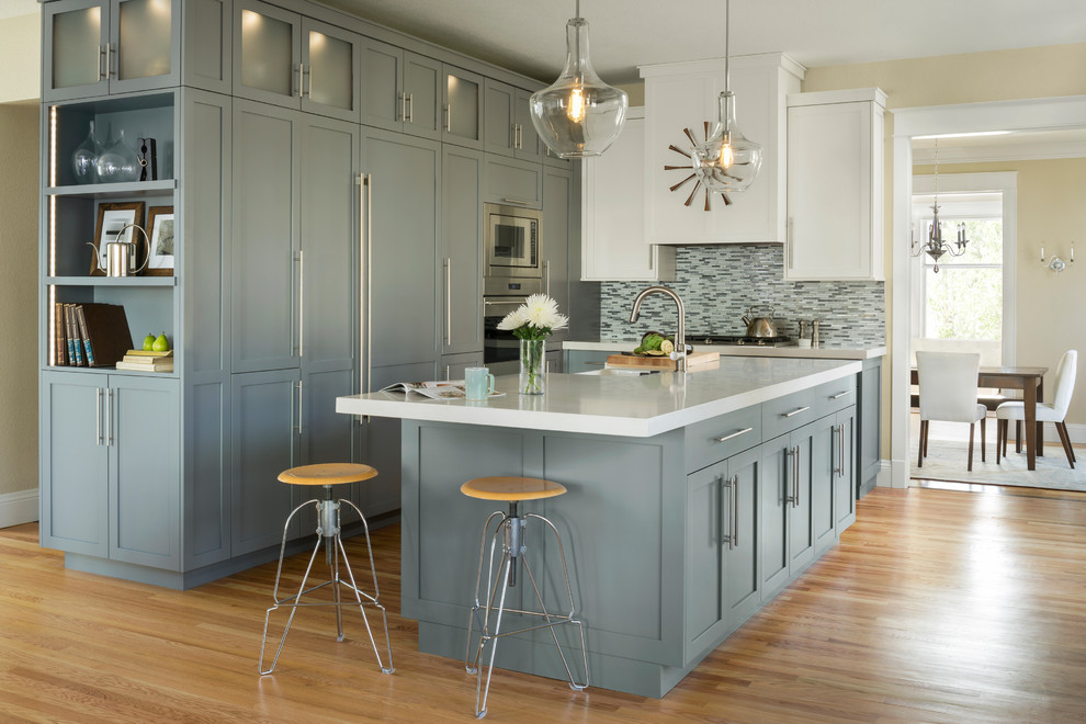 Klassische Küche in grau-weiß mit Kücheninsel, Landhausspüle, Schrankfronten im Shaker-Stil, grauen Schränken, bunter Rückwand, Rückwand aus Stäbchenfliesen, Küchengeräten aus Edelstahl und hellem Holzboden in Denver