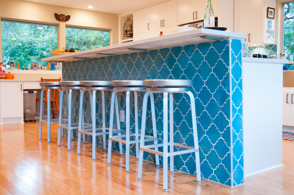 Example of a mid-sized trendy u-shaped light wood floor eat-in kitchen design in Austin with a farmhouse sink, flat-panel cabinets, white cabinets, quartzite countertops, blue backsplash, ceramic backsplash, stainless steel appliances and an island