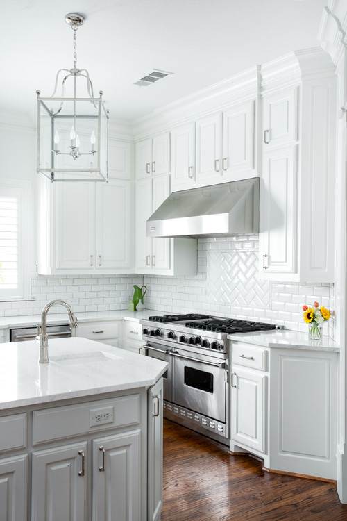 All white L-shaped kitchen with bright subway tile backsplash and a dark wood hardwood flooring. Stainless steel stove, rangehood, and hardware.