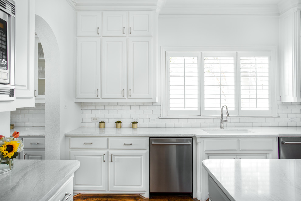 Inspiration for a mid-sized timeless u-shaped medium tone wood floor and brown floor enclosed kitchen remodel in Dallas with an undermount sink, raised-panel cabinets, white cabinets, quartz countertops, white backsplash, ceramic backsplash, stainless steel appliances, an island and white countertops