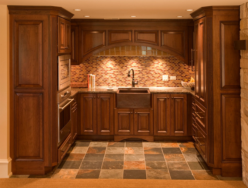 Exempel på ett avskilt, litet klassiskt u-kök, med en rustik diskho, luckor med upphöjd panel, bruna skåp, granitbänkskiva, flerfärgad stänkskydd, glaspanel som stänkskydd och rostfria vitvaror