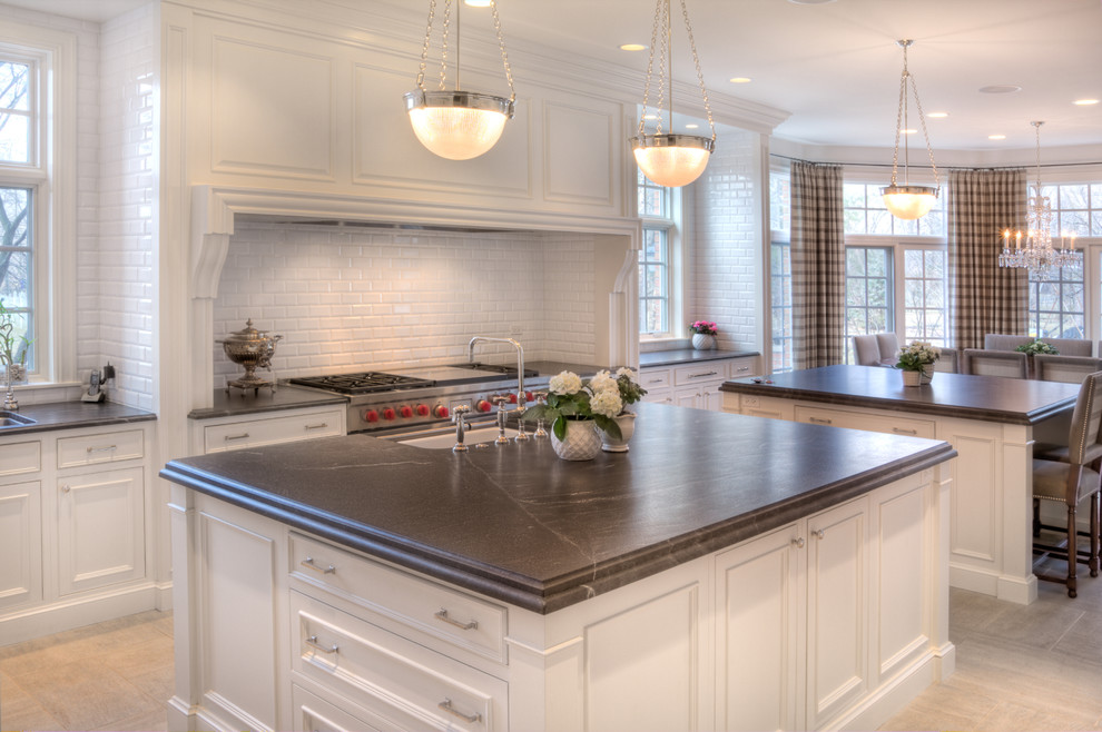 Large transitional u-shaped slate floor eat-in kitchen photo in Chicago with a farmhouse sink, recessed-panel cabinets, white cabinets, white backsplash, stainless steel appliances, two islands, soapstone countertops and subway tile backsplash