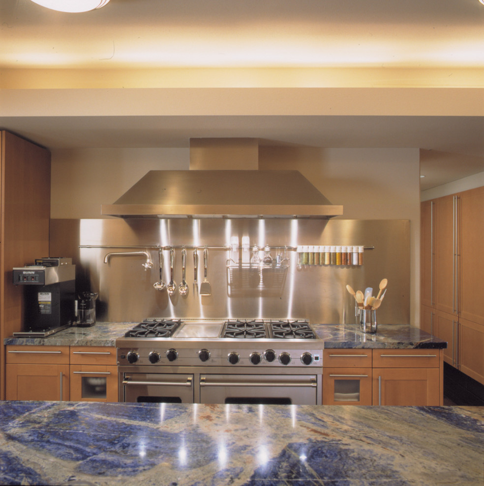 Diseño de cocina contemporánea con puertas de armario de madera clara, salpicadero metalizado, electrodomésticos de acero inoxidable y encimeras azules
