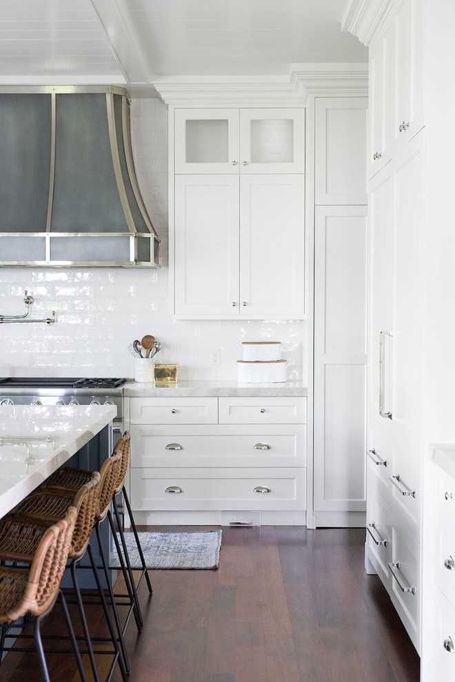 Klassisk inredning av ett stort vit vitt l-kök, med en rustik diskho, skåp i shakerstil, blå skåp, vitt stänkskydd, stänkskydd i tunnelbanekakel, rostfria vitvaror, mörkt trägolv och en köksö
