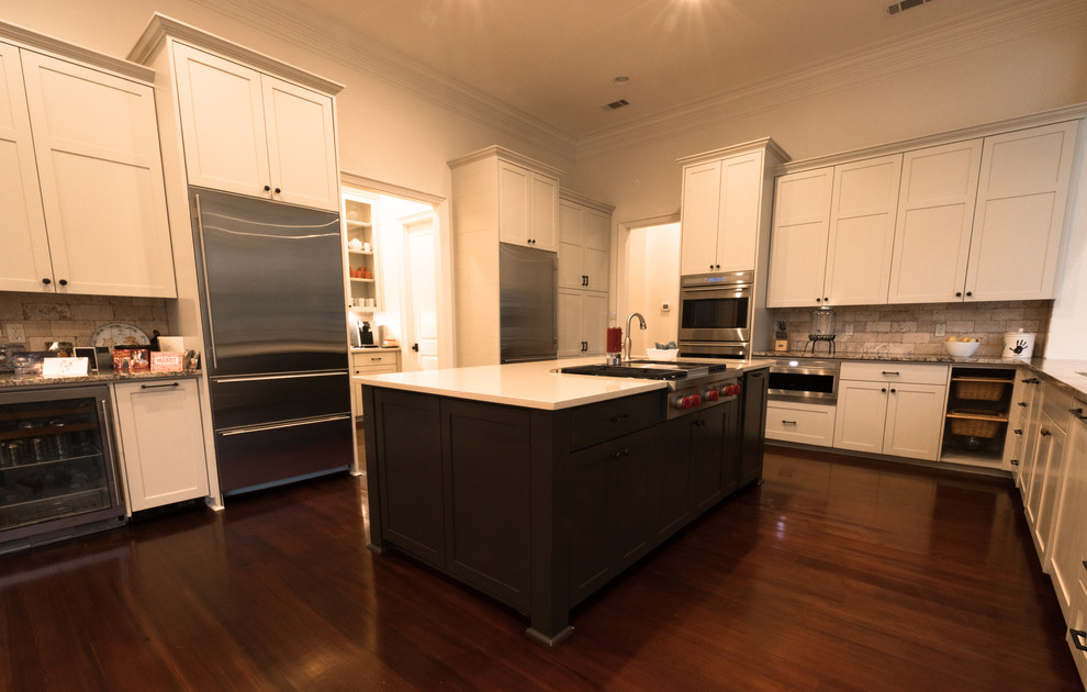 Design ideas for a large traditional u-shaped open plan kitchen in New Orleans with a submerged sink, shaker cabinets, white cabinets, grey splashback, stone tiled splashback, stainless steel appliances, dark hardwood flooring and an island.