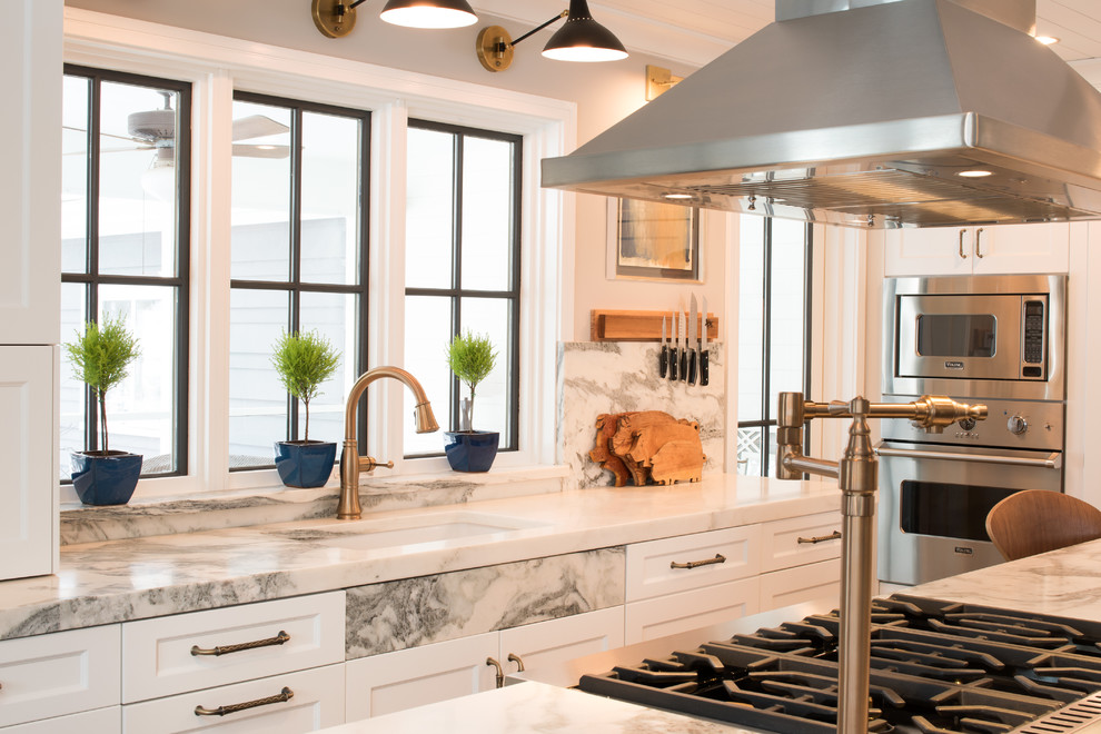 Medium sized classic galley kitchen/diner in Minneapolis with a submerged sink, flat-panel cabinets, white cabinets, marble worktops, white splashback, marble splashback, stainless steel appliances, dark hardwood flooring, an island, brown floors and white worktops.