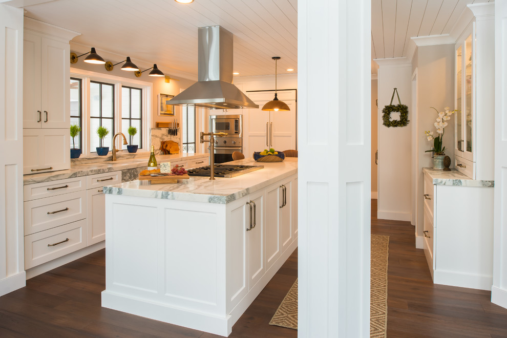 Bild på ett mellanstort vintage vit vitt kök, med en undermonterad diskho, släta luckor, vita skåp, marmorbänkskiva, vitt stänkskydd, stänkskydd i marmor, rostfria vitvaror, mörkt trägolv, en köksö och brunt golv