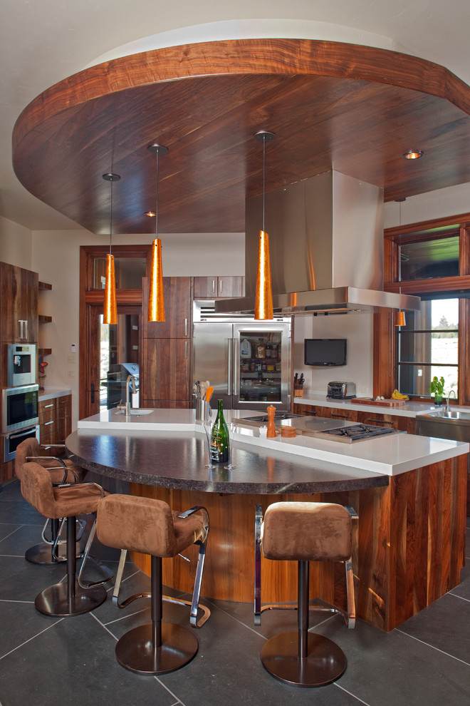 Foto på ett stort amerikanskt kök, med en undermonterad diskho, släta luckor, skåp i mellenmörkt trä, bänkskiva i kvartsit, vitt stänkskydd, stänkskydd i sten, rostfria vitvaror, skiffergolv, en köksö och grått golv