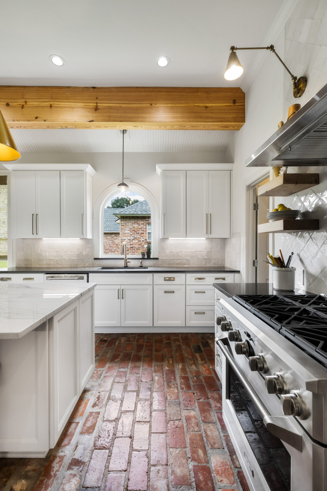 Inredning av ett stort grå grått kök, med en undermonterad diskho, luckor med infälld panel, vita skåp, bänkskiva i kvartsit, vitt stänkskydd, stänkskydd i tunnelbanekakel, rostfria vitvaror, tegelgolv, en köksö och brunt golv