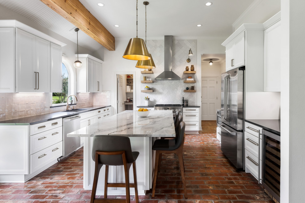 Exempel på ett stort grå grått kök, med en undermonterad diskho, luckor med infälld panel, vita skåp, bänkskiva i kvartsit, vitt stänkskydd, stänkskydd i tunnelbanekakel, rostfria vitvaror, tegelgolv, en köksö och brunt golv