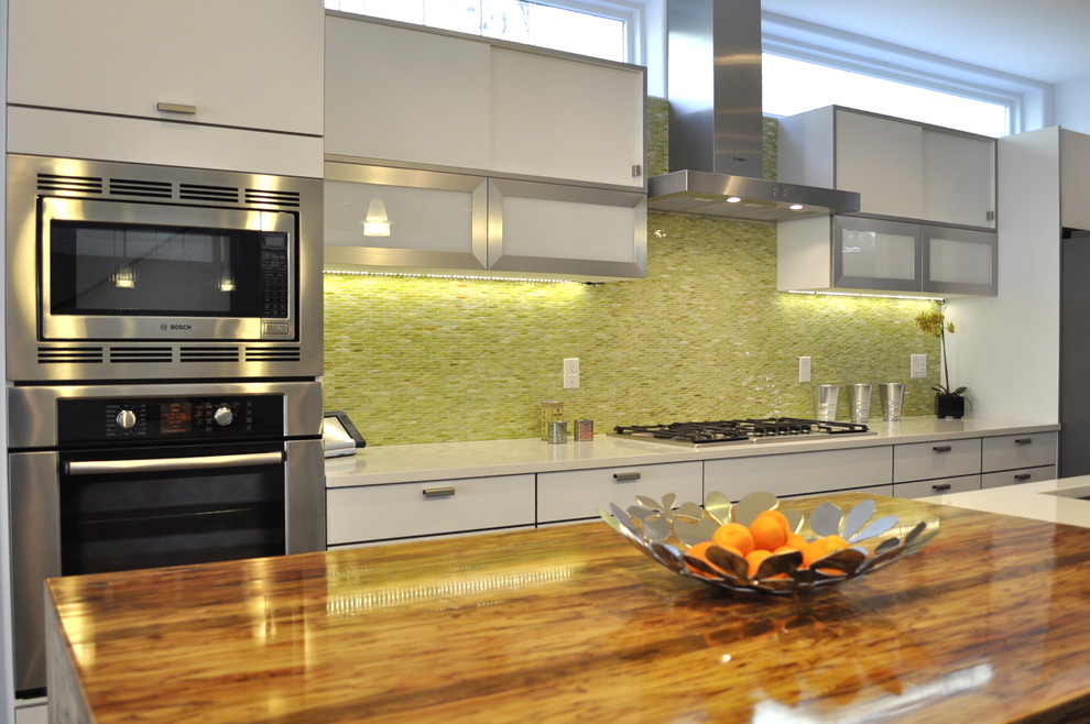 Inredning av ett modernt avskilt, stort linjärt kök, med en undermonterad diskho, släta luckor, vita skåp, bänkskiva i koppar, grönt stänkskydd, stänkskydd i mosaik, rostfria vitvaror, mellanmörkt trägolv, en köksö och brunt golv