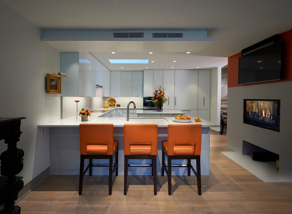 Bild på ett mellanstort funkis kök, med en undermonterad diskho, luckor med glaspanel, vita skåp, bänkskiva i kvarts, grått stänkskydd, stänkskydd i sten, integrerade vitvaror, ljust trägolv och en köksö