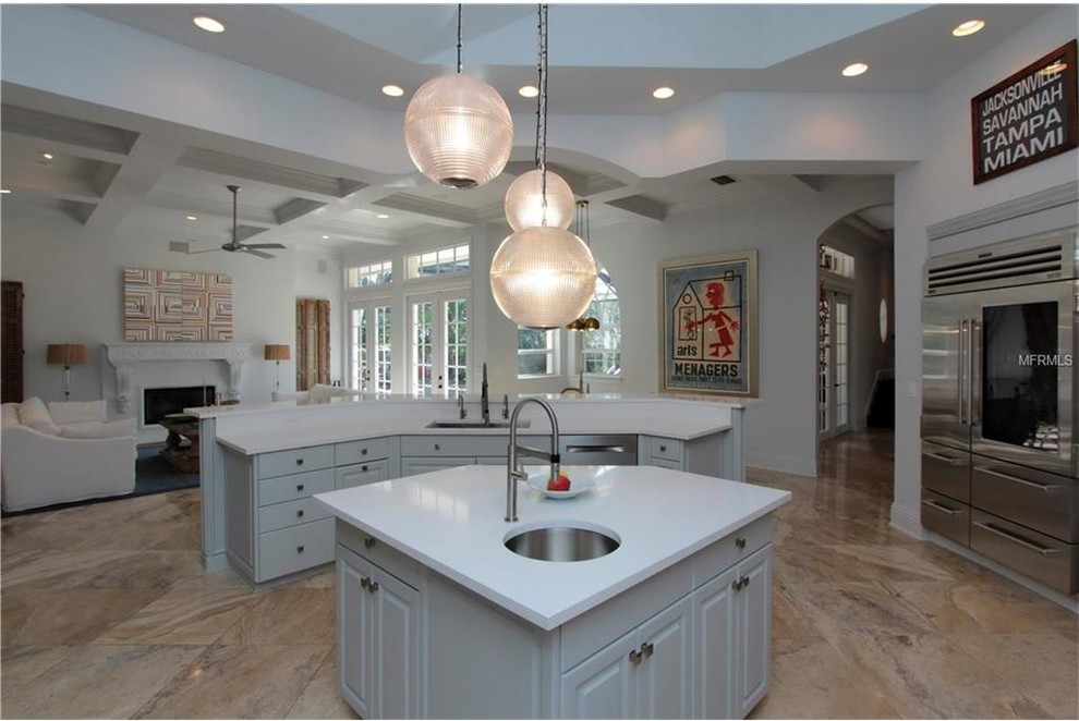 This is an example of a large victorian u-shaped open plan kitchen in Tampa with a submerged sink, raised-panel cabinets, white cabinets, quartz worktops, white splashback, stainless steel appliances, travertine flooring, multiple islands and beige floors.