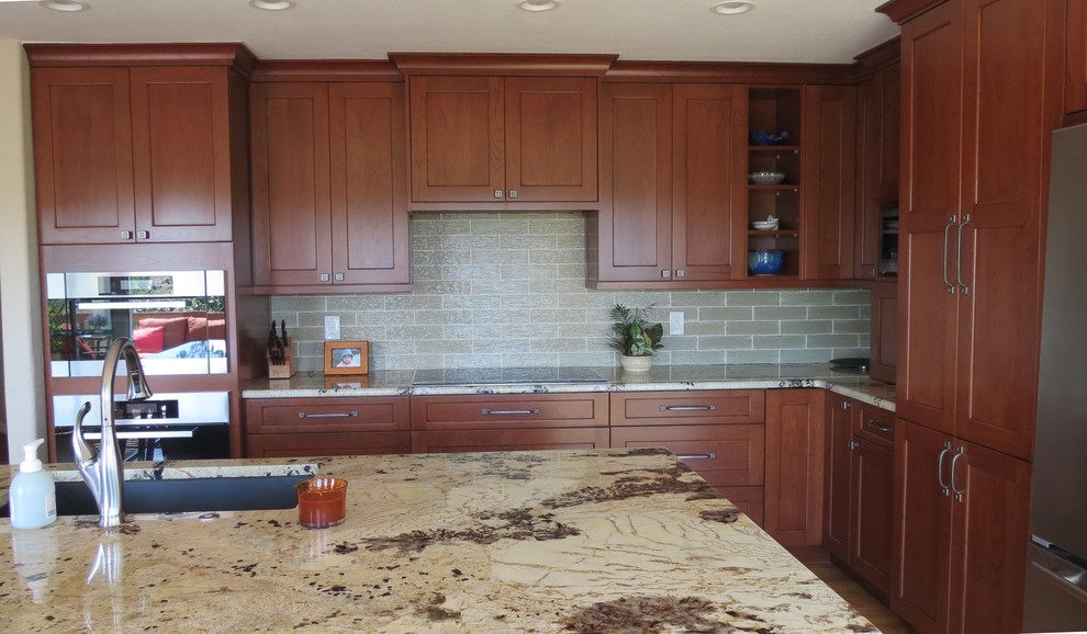 Medium sized traditional l-shaped open plan kitchen in Denver with a single-bowl sink, recessed-panel cabinets, medium wood cabinets, granite worktops, green splashback, glass tiled splashback, stainless steel appliances, light hardwood flooring and an island.