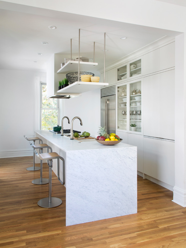 Medium sized contemporary galley enclosed kitchen in Denver with a submerged sink, marble worktops, white splashback, medium hardwood flooring, an island, brown floors, white worktops, flat-panel cabinets, white cabinets and stainless steel appliances.