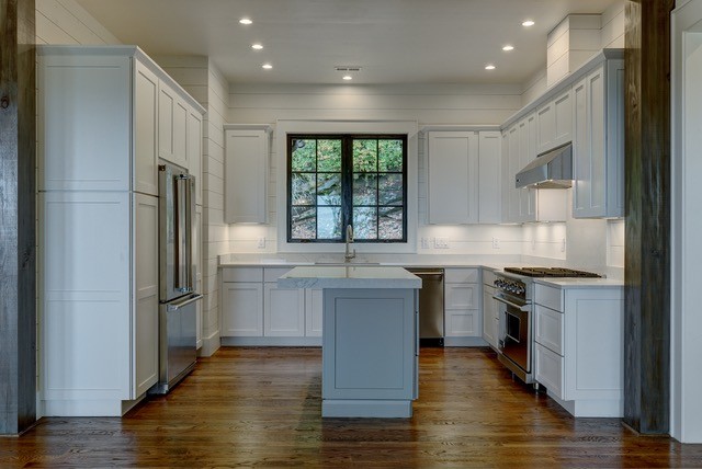 Photo of a medium sized rustic u-shaped kitchen in Other with a submerged sink, shaker cabinets, white cabinets, engineered stone countertops, white splashback, wood splashback, stainless steel appliances, medium hardwood flooring, an island and brown floors.