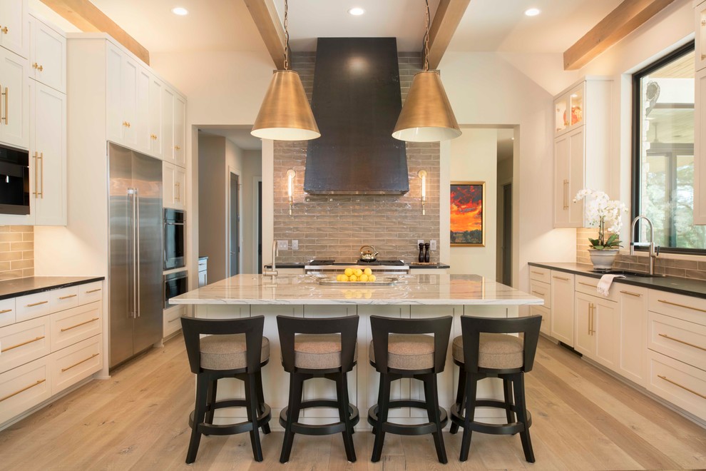 Example of a transitional light wood floor and beige floor kitchen design in Austin with shaker cabinets, white cabinets, an island, gray backsplash, stainless steel appliances and black countertops