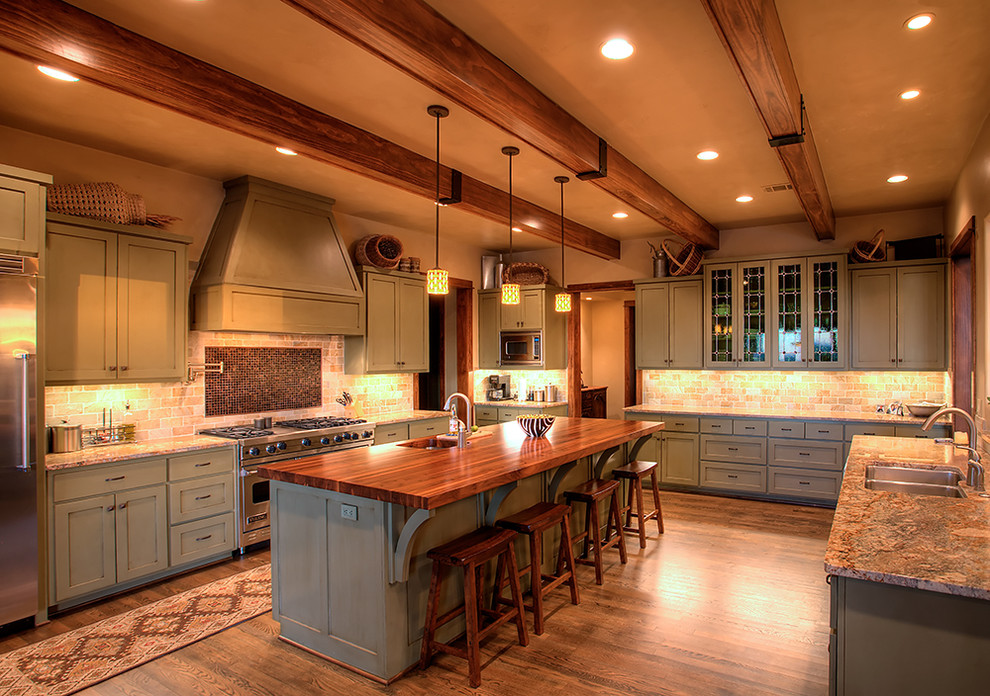 Example of a mountain style kitchen design in Austin with stainless steel appliances, stone tile backsplash and wood countertops