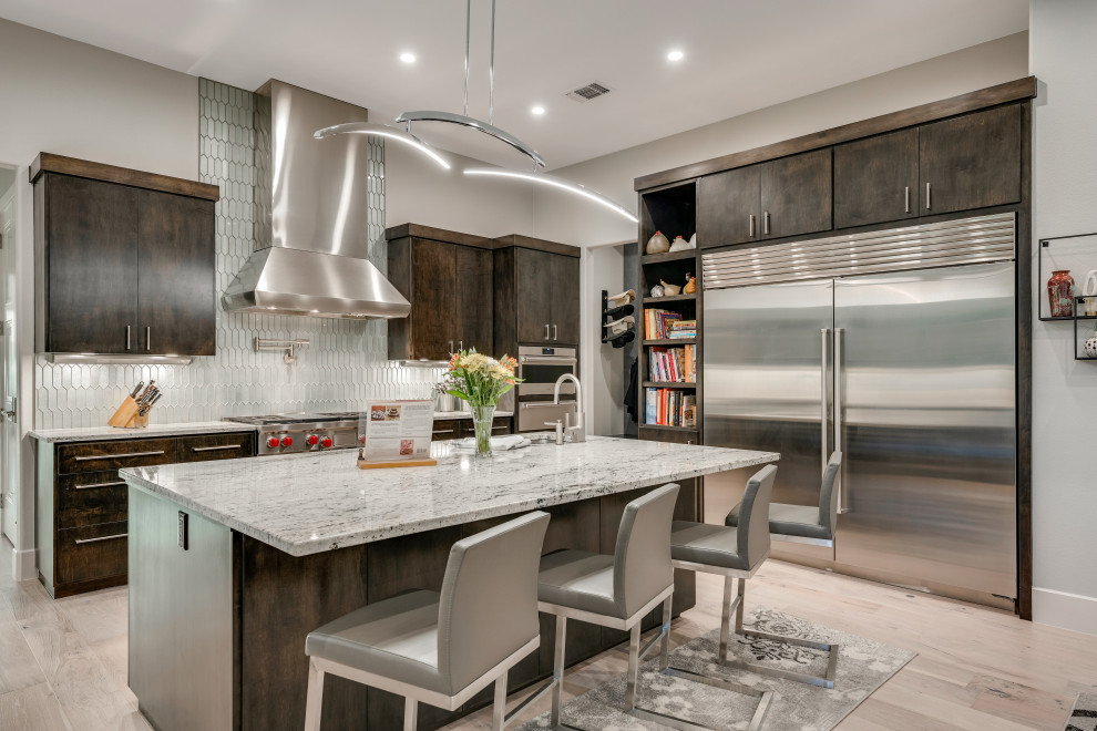 Photo of a contemporary l-shaped kitchen in Austin with flat-panel cabinets, dark wood cabinets, grey splashback, mosaic tiled splashback, stainless steel appliances, light hardwood flooring, an island, beige floors and grey worktops.