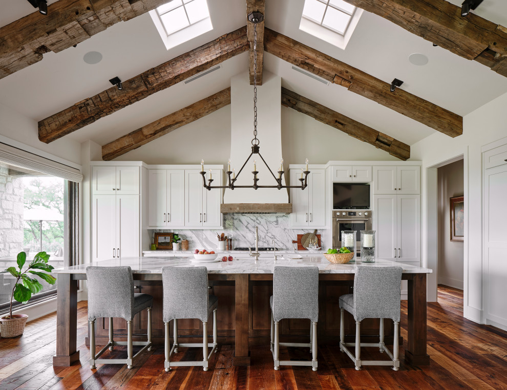 Photo of an expansive rural single-wall kitchen in Austin with shaker cabinets, white cabinets, stainless steel appliances, medium hardwood flooring, an island and exposed beams.