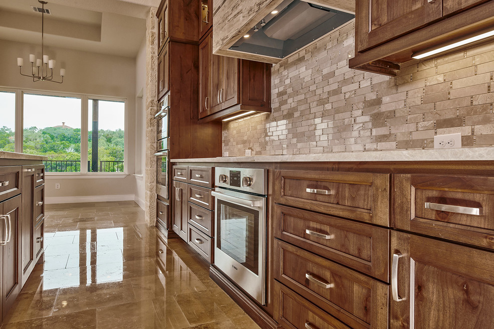 Exempel på ett mellanstort klassiskt beige beige kök och matrum, med en undermonterad diskho, luckor med infälld panel, bruna skåp, träbänkskiva, beige stänkskydd, stänkskydd i marmor, rostfria vitvaror, marmorgolv, en köksö och beiget golv