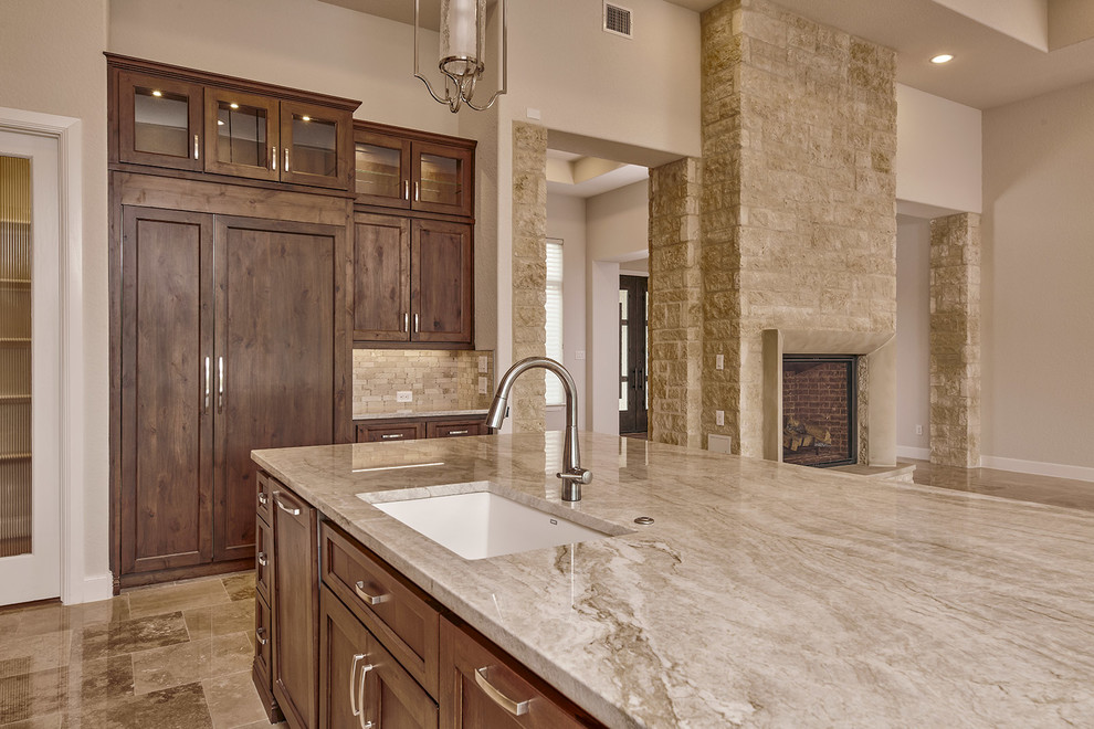 Klassisk inredning av ett mellanstort beige beige kök och matrum, med en undermonterad diskho, luckor med infälld panel, bruna skåp, träbänkskiva, beige stänkskydd, stänkskydd i marmor, rostfria vitvaror, marmorgolv, en köksö och beiget golv