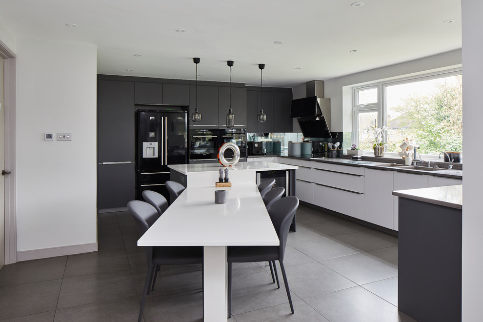 Moderne Küche in U-Form mit Unterbauwaschbecken, flächenbündigen Schrankfronten, weißen Schränken, schwarzen Elektrogeräten, Kücheninsel, grauem Boden und grauer Arbeitsplatte in London