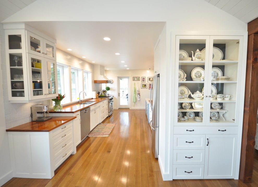Bild på ett stort funkis kök, med en undermonterad diskho, skåp i shakerstil, vita skåp, träbänkskiva, vitt stänkskydd, stänkskydd i porslinskakel, rostfria vitvaror, mellanmörkt trägolv och en halv köksö