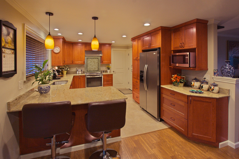 Aménagement d'une cuisine américaine encastrable classique en bois brun avec un placard avec porte à panneau encastré, un plan de travail en granite, une crédence beige et une péninsule.