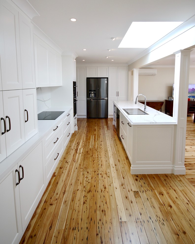 Inspiration for a large classic u-shaped open plan kitchen in Sydney with a built-in sink, recessed-panel cabinets, white cabinets, engineered stone countertops, white splashback, stone slab splashback, stainless steel appliances, medium hardwood flooring, an island, brown floors and white worktops.