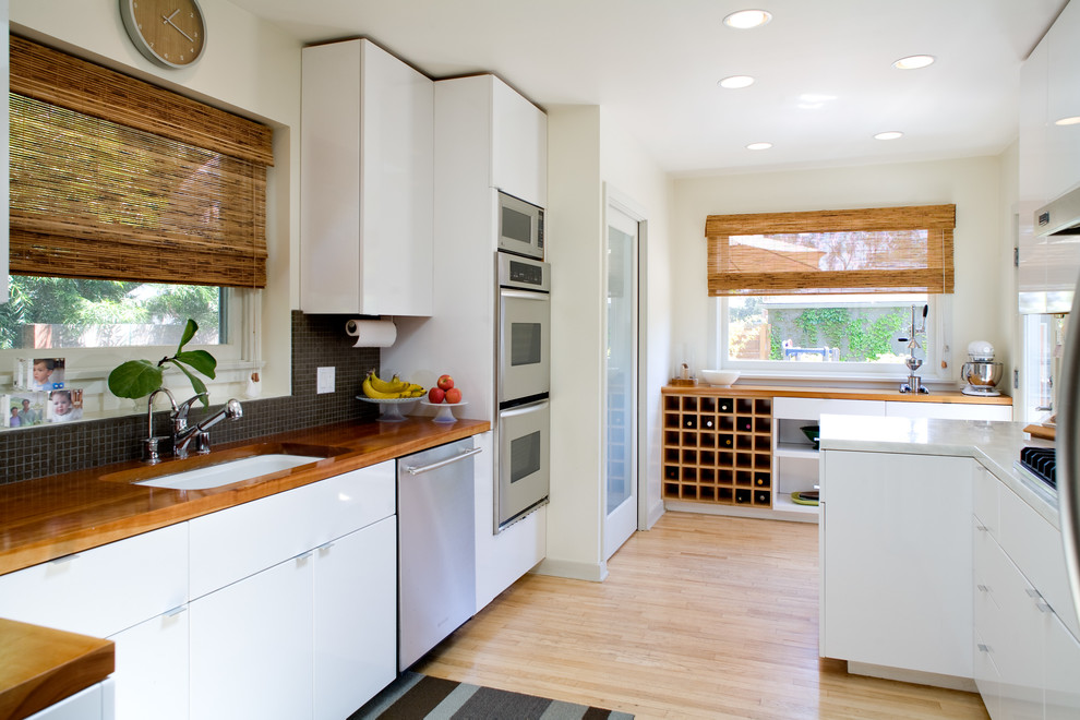 Moderne Küche mit Unterbauwaschbecken, flächenbündigen Schrankfronten, weißen Schränken, Küchenrückwand in Schwarz und Küchengeräten aus Edelstahl in Los Angeles