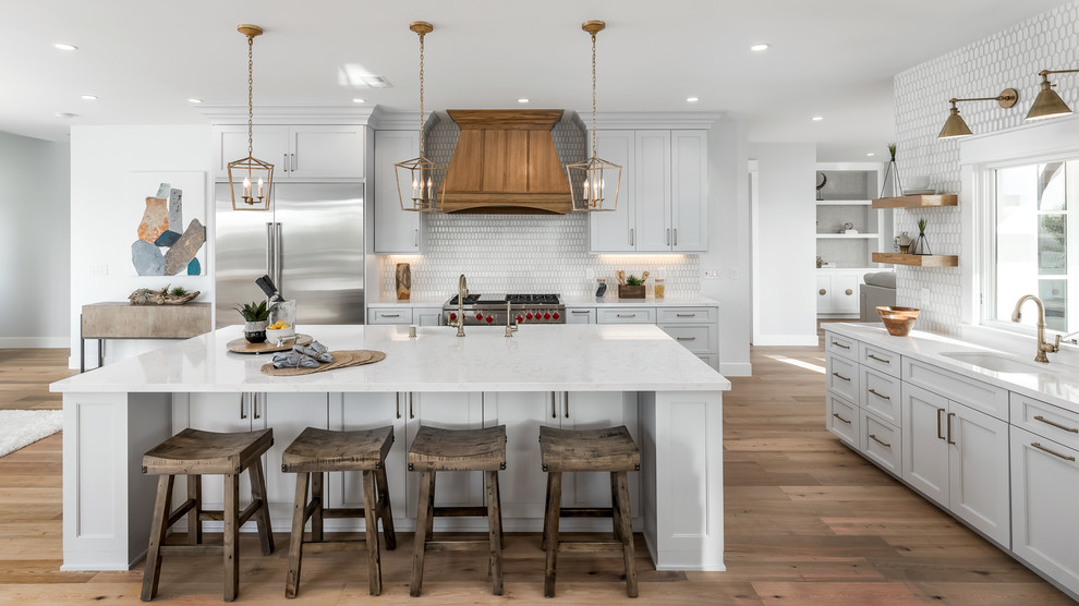 Foto de cocina de estilo de casa de campo grande con puertas de armario blancas, salpicadero blanco, electrodomésticos de acero inoxidable, suelo de madera en tonos medios, una isla, suelo marrón, encimeras blancas, fregadero sobremueble, armarios estilo shaker y encimera de cuarzo compacto